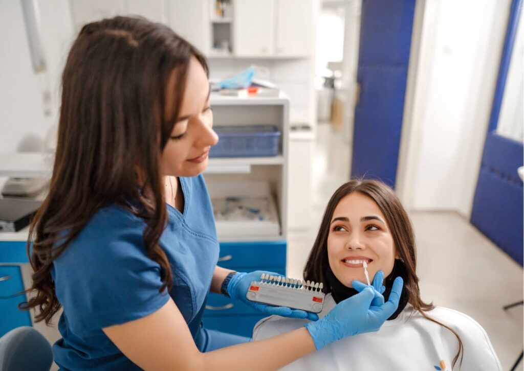 Dentist comparing tooth shade samples during a cosmetic consultation to help a patient choose between veneers and Lumineers.